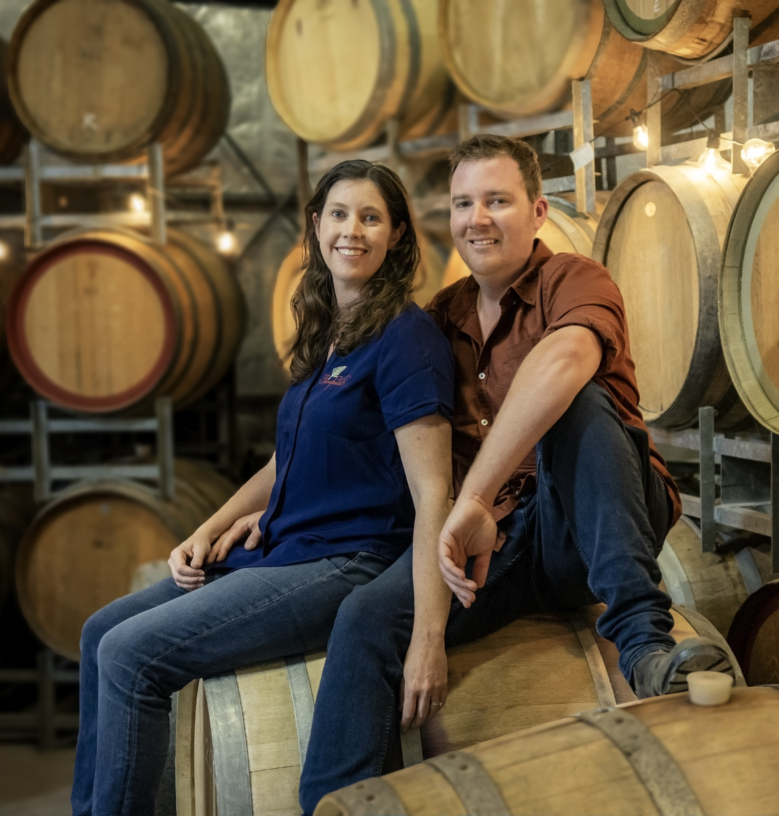 Man and woman sitting on top a wine barrel 
